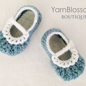 May include: A pair of blue crocheted baby shoes with white crocheted trim and straps. The shoes have a scalloped edge and are made with a textured stitch.
