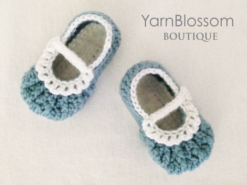 May include: A pair of blue crocheted baby shoes with white crocheted trim and straps. The shoes have a scalloped edge and are made with a textured stitch.