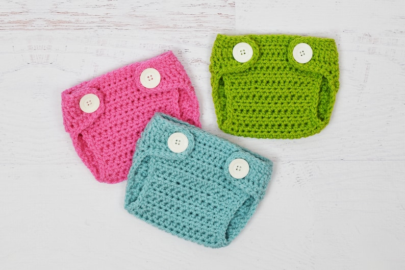 May include: Three crocheted baby diaper covers in pink, green, and blue with white buttons.