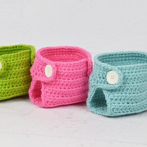 May include: Three crocheted baby diaper covers in green, pink, and blue with white buttons.