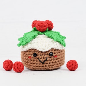 May include: A crocheted Christmas pudding plush toy with a smiling face, red berries, and green holly leaves.