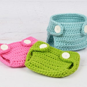 May include: Three crocheted baby diaper covers in pink, green, and light blue with white buttons.