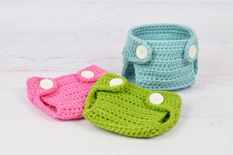 May include: Three crocheted baby diaper covers in pink, green, and light blue with white buttons.
