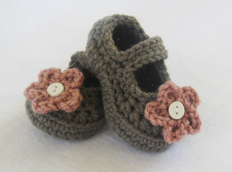 May include: A pair of brown crocheted baby shoes with pink flower embellishments and white buttons.