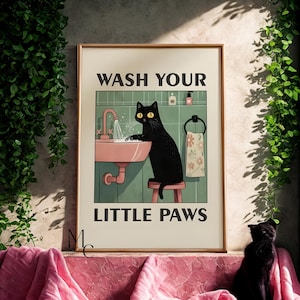 Può includere: Una stampa artistica incorniciata con un gatto nero che si lava le zampe in un lavandino rosa. Il testo "WASH YOUR LITTLE PAWS" è sopra e sotto l'illustrazione del gatto. Tema bagno umoristico.