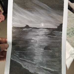 Puede incluir: Una pintura de acuarela en escala de grises de un paisaje marino. La obra de arte representa un océano iluminado por la luna con reflejos blancos que reflejan la luz de la luna. El cielo es oscuro con pinceladas blancas, y la pintura está sobre papel blanco.