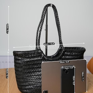 May include: Black woven tote bag with braided handles. The bag is 23cm high, 40cm wide, and 11cm deep. A tablet and phone are placed next to the bag for size comparison. The tablet is 26cm long. The bag's height is 9.1 inches.