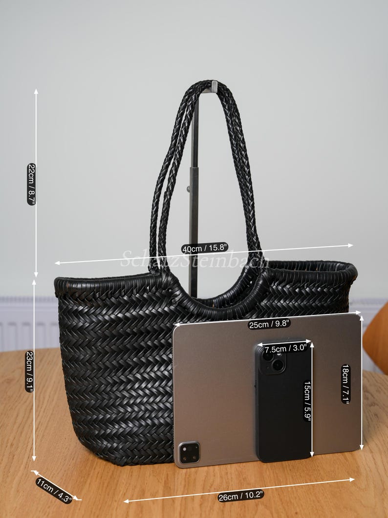 May include: Black woven tote bag with braided handles. The bag is 23cm high, 40cm wide, and 11cm deep. A tablet and phone are placed next to the bag for size comparison. The tablet is 26cm long. The bag's height is 9.1 inches.