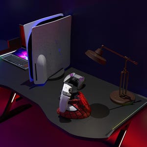 May include: A gaming setup with a black desk, a white and black gaming console, a laptop, and two white game controllers. A brown desk lamp is also on the desk. The console is in a vertical position.