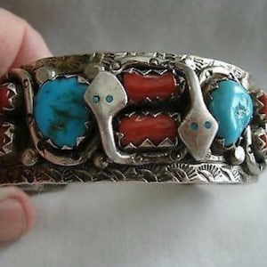 May include: A silver bracelet with turquoise and coral stones. The bracelet is decorated with a snake design.