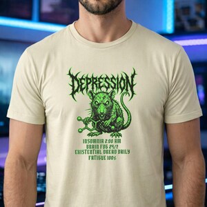 Puede incluir: Camiseta beige con un gr&aacute;fico verde. El gr&aacute;fico incluye la palabra "DEPRESSION" en una fuente puntiaguda sobre una rata verde que sostiene una estructura molecular. Debajo, las frases "INSOMNIA 2:00 AM", "BRAIN FOG 24/7", "EXISTENTIAL DREAD DAILY" y "FATIGUE 100%."