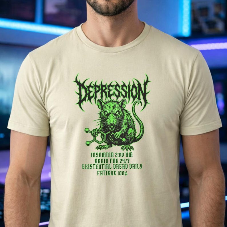 Puede incluir: Camiseta beige con un gr&aacute;fico verde. El gr&aacute;fico incluye la palabra "DEPRESSION" en una fuente puntiaguda sobre una rata verde que sostiene una estructura molecular. Debajo, las frases "INSOMNIA 2:00 AM", "BRAIN FOG 24/7", "EXISTENTIAL DREAD DAILY" y "FATIGUE 100%."
