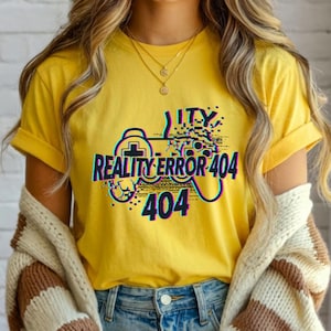 Può includere: T-shirt giallo con la scritta "REALITY ERROR 404" e una grafica di controller. Il design presenta un effetto glitch con accenti blu e verdi. La maglietta è a maniche corte.