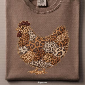 May include: Espresso-colored t-shirt featuring a patchwork chicken design. The chicken is composed of various leopard print patterns, with rhinestone accents. The shirt has a crew neck and short sleeves. The text "Espresso" is at the bottom.