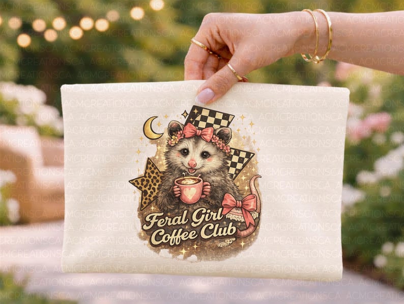 May include: A cream-colored pouch featuring a possum illustration with a floral crown, holding a coffee cup. The text "Feral Girl Coffee Club" is below the possum. The design includes a checkered flag and a crescent moon.