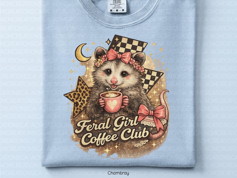 May include: Light blue t-shirt featuring a possum illustration. The possum wears a floral crown and holds a coffee cup with a heart. The text "Feral Girl Coffee Club" is below the possum. The design includes a star, moon, and checkered flag.