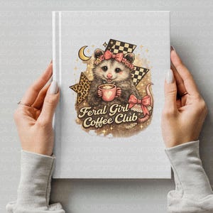 May include: A notebook with a whimsical illustration of an opossum holding a coffee cup, adorned with a floral headband and a pink bow. The text "Feral Girl Coffee Club" is featured below the opossum. The design includes a star and checkered flag.