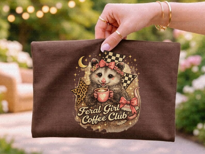 May include: A brown zippered pouch featuring a cartoon opossum holding a coffee cup, adorned with a floral crown and bow. The text "Feral Girl Coffee Club" is displayed below the opossum. The design includes a star, moon, and checkered flag.
