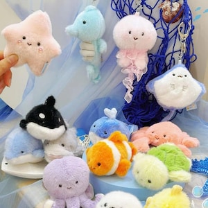 May include: A selection of soft toy keyrings featuring various sea creatures. These include a pink starfish, a blue seahorse, and a jellyfish with pink frills. Other creatures include a whale, clownfish, and a stingray. The keyrings are colourful.