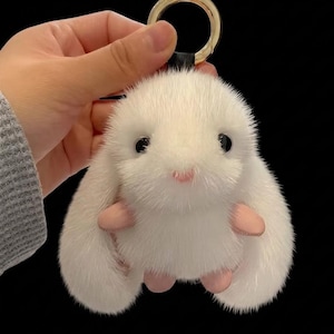 May include: A white fluffy bunny keyring with a gold-coloured ring. The keyring has a black leather strap and pink paws and nose. The bunny's eyes are black and it has a cute, cartoonish appearance.