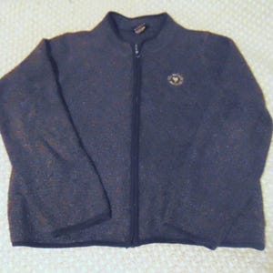 May include: A dark blue fleece jacket with a full-length zipper and a small emblem on the chest. The jacket has a high collar and long sleeves. The fabric has a speckled texture.