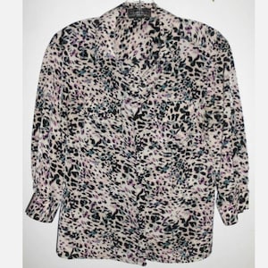 May include: A long-sleeved blouse with a cream-colored background and a black, purple, and teal animal print pattern. The blouse has a collared neckline and button-down front. The sleeves have buttoned cuffs.