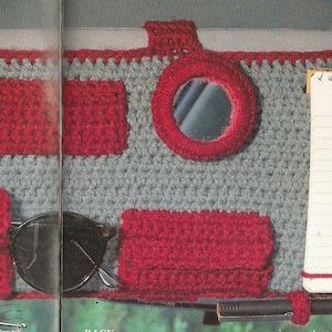 May include: A gray and red crocheted car visor organizer with multiple pockets and a small mirror. The organizer has a pocket for sunglasses, a pocket for a comb, a pocket for a notepad, and a pocket for tissues. The organizer also has a small mirror and a hook for hanging keys.