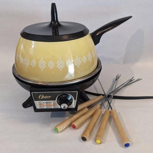 May include: A yellow Oster electric fondue pot with a black lid, handle, and base. The pot features a white decorative pattern and a control dial labeled Oster electric fondue. Five metal fondue forks with wooden handles and colored ends are included.