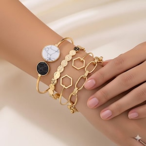 May include: A collection of gold-toned bracelets. One bracelet features a white marble-like stone, another a black marble-like stone. Other bracelets have geometric and chain link designs. The bracelets are worn on a wrist.