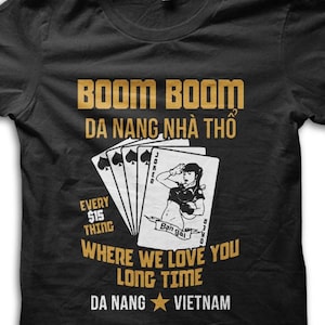 May include: Black t-shirt with gold text and a playing card design. The text includes "BOOM BOOM DA NANG NHÀ THÔ", "EVERY $15 THING", and "WHERE WE LOVE YOU LONG TIME DA NANG VIETNAM". The design features a woman on a playing card.
