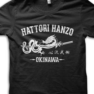 May include: Black t-shirt with a white graphic featuring the text "HATTORI HANZO" above a dragon and sword design. Below the graphic are Japanese characters and the word "OKINAWA".
