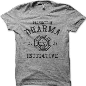 Puede incluir: Camiseta gris con el texto "PROPERTY OF DHARMA INITIATIVE", un logotipo de Dharma y los números "1977". La camiseta tiene cuello redondo y mangas cortas.