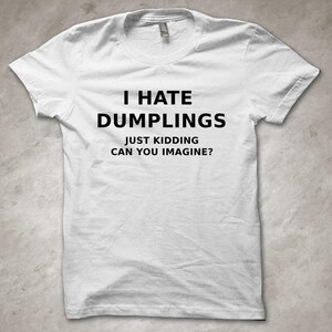 May include: White t-shirt featuring the black text: "I HATE DUMPLINGS JUST KIDDING CAN YOU IMAGINE?" The shirt has a crew neck and short sleeves.