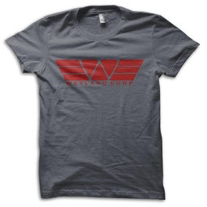 Könnte beinhalten: Ein graues T-Shirt mit einem roten Weyland Corp Logo. Das Logo ist ein stilisiertes Design mit dem Text "WEYLAND CORP" darunter. Das T-Shirt besteht aus einem weichen Material.