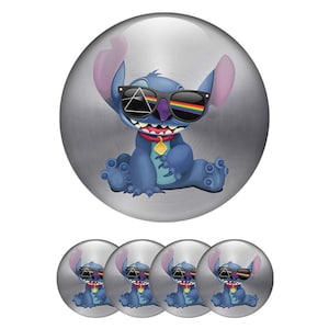 Op de afbeelding: Een ronde metalen badge met een blauw buitenaards personage dat een zwarte zonnebril draagt. De glazen tonen een wit driehoekig prisma en een regenboogspectrum. Het personage heeft grote oren en een rode halsband met een gele hanger.