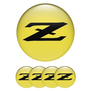 Könnte beinhalten: Ein Satz von fünf gelb-schwarzen runden Emblemen. Die Embleme haben eine glänzende Oberfläche und ein stilisiertes schwarzes "Z"-Design. Das größte Emblem befindet sich über vier kleineren, identischen Emblemen.
