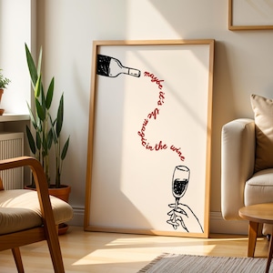 Può includere: Una stampa artistica incorniciata con un'illustrazione in bianco e nero di una bottiglia di vino che versa in un calice tenuto da una mano. La frase "maybe it's the magic in the wine" è scritta in rosso. L'opera è esposta in un soggiorno.
