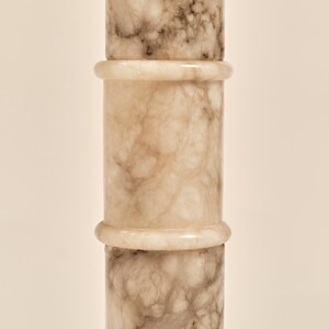 May include: A vertical, cylindrical object with a marble-like appearance. The object is composed of three stacked sections, each with a light beige base color and veining in shades of brown and gray. The sections are separated by a lighter, ring-shaped detail.