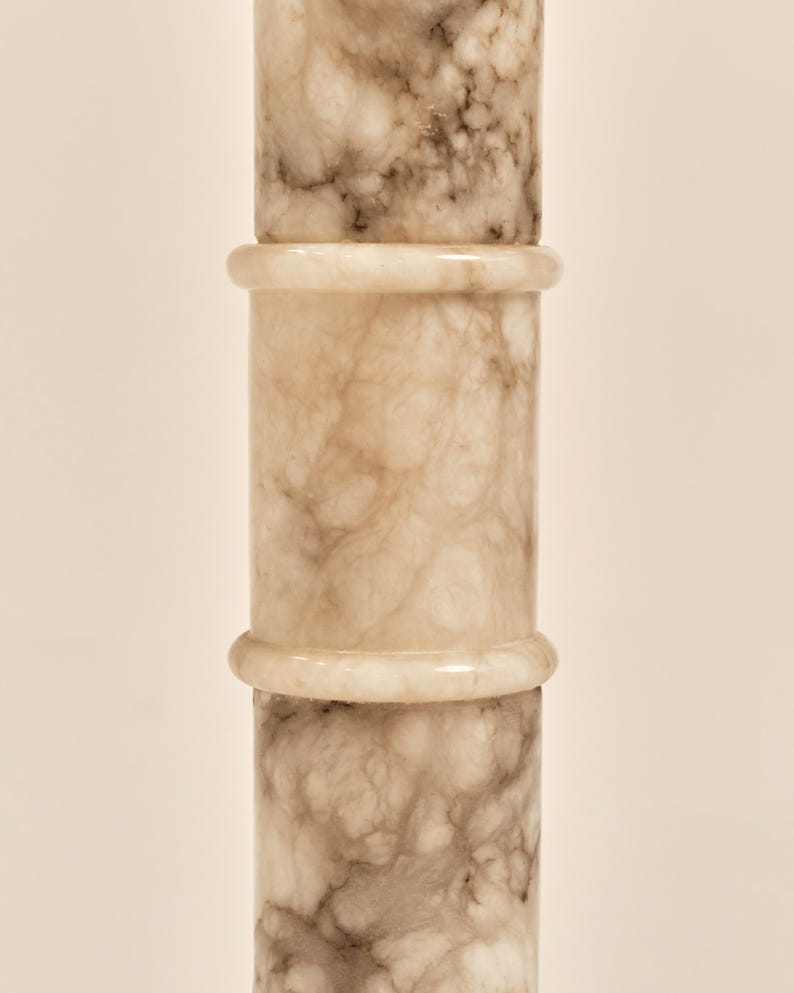 May include: A vertical, cylindrical object with a marble-like appearance. The object is composed of three stacked sections, each with a light beige base color and veining in shades of brown and gray. The sections are separated by a lighter, ring-shaped detail.