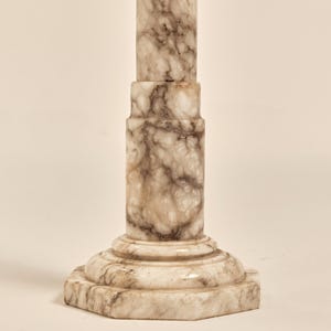 May include: A marble column with a light beige and brown veined pattern. The column has a hexagonal base and a cylindrical shaft. The column is approximately 30 inches tall.