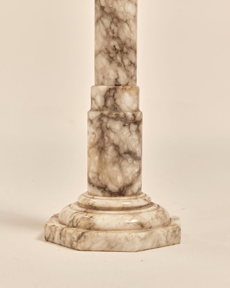 May include: A marble column with a light beige and brown veined pattern. The column has a hexagonal base and a cylindrical shaft. The column is approximately 30 inches tall.