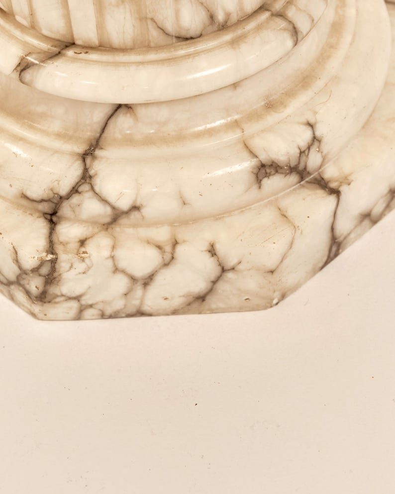 May include: Close-up of a decorative, off-white marble object with brown veining. The object has a rounded, tiered design with a hexagonal base. The marble has a polished, glossy finish.