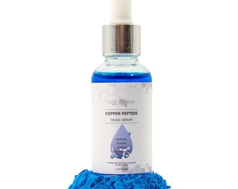 May include: A clear glass bottle of Cell Revive Copper Peptide Facial Serum with a silver dropper top. The bottle contains a blue liquid and sits on a bed of blue powder. The label includes the words "Copper Peptide Facial Serum".