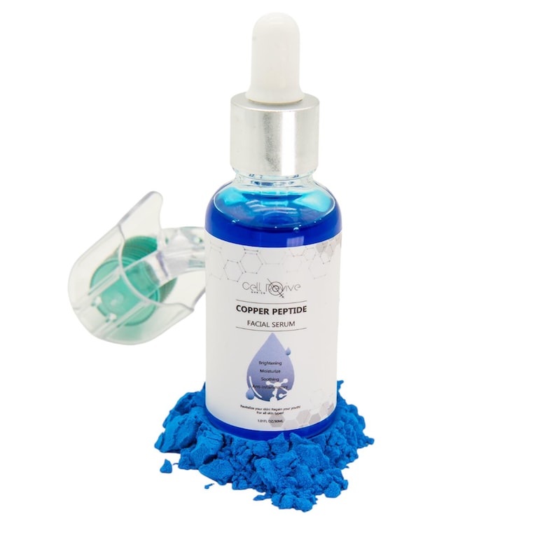 May include: A bottle of Cell Revive Copper Peptide Facial Serum with a silver cap and white dropper. The bottle is surrounded by blue powder. The label reads "Copper Peptide Facial Serum" with a graphic of water droplets.