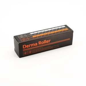 May include: A black rectangular box labeled "Derma Roller" in orange text. The box has a series of numbers and measurements printed on the top, and instructions on the side. The box is on a white background.