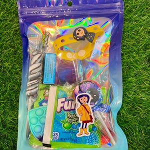 May include: A clear, iridescent bag filled with candy and small toys. Items include a yellow bracelet with a character design, a blue and green pop-it toy, and a lollipop. The bag contains a variety of colorful treats and a sticker.