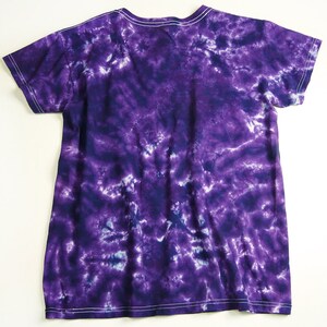 Puede incluir: Camiseta de color morado con estampado tie-dye, cuello en V y mangas cortas.