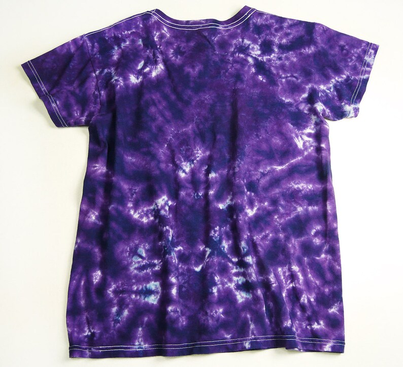 Puede incluir: Camiseta de color morado con estampado tie-dye, cuello en V y mangas cortas.