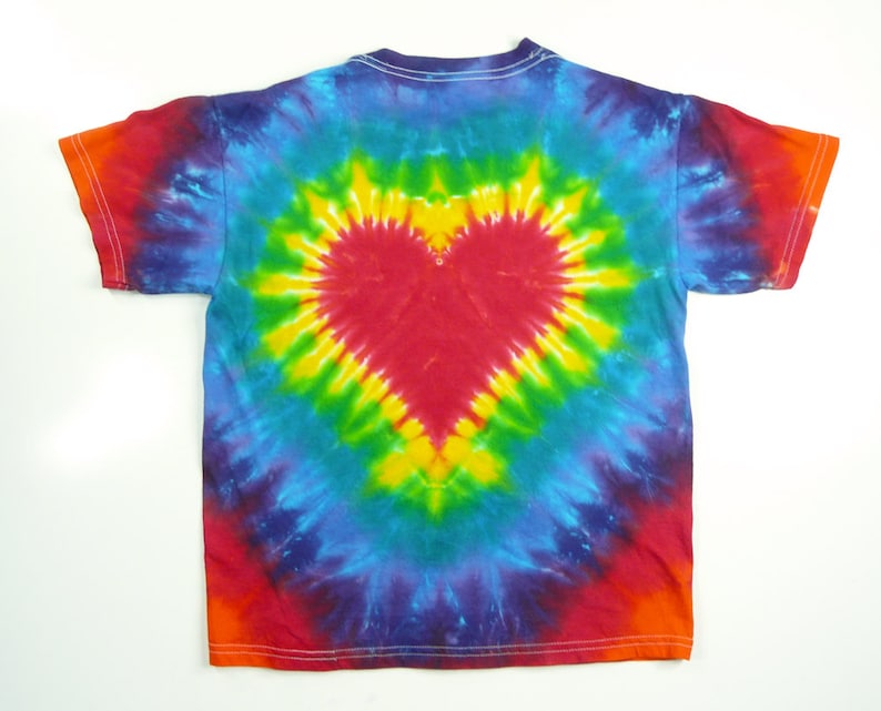 May include: A tie-dye t-shirt with a red heart design in the centre. The shirt is a rainbow of colours, including blue, green, yellow, orange, and red.