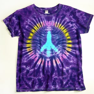 Puede incluir: Camiseta de color morado con estampado tie-dye con un s&iacute;mbolo de paz azul en el centro. El s&iacute;mbolo de paz est&aacute; rodeado por un c&iacute;rculo amarillo y rosa.